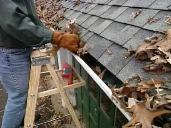 man standing on ladders and cleaning gutters
