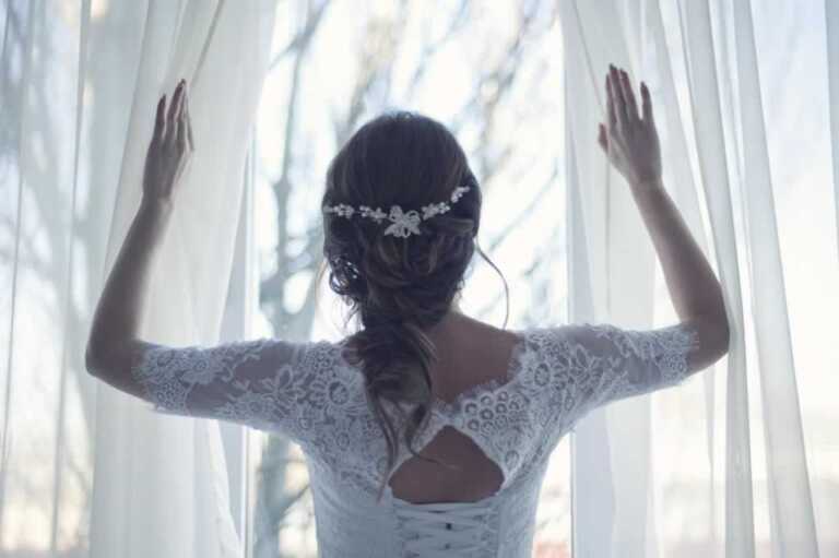 woman in wedding dress opening curtains