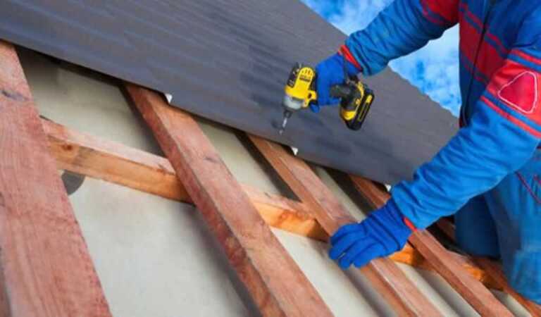 roofing contractor screwing metal roof with cordless drill